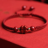 Red braided cord bracelet with cinnabar four-leaf clover charm, gold accent beads and round red stone beads on matching red fabric background