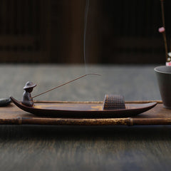 Fisherman Incense Burner – Ceramic boat with hat figure on bamboo mat, blossoms nearby, zen art