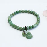 Stretch beaded bracelet with polished cyan jade beads, carved Laughing Buddha pendant and jade bi disc charm on white background with soft pink bokeh accent