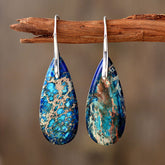Emperor Stone Healing Crystal Earrings – Teardrop natural stone earrings with royal blue turquoise-green veins and silver hooks on driftwood prop