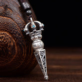 Tibetan Dorje Vajra Rotatable Pendant – Antiqued silver with turquoise inlays, lotus motifs and Sanskrit engravings on dark cord, dark wood vessel backdrop