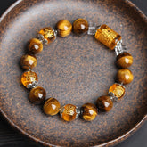 Tiger eye beaded stretch bracelet with carved amber fortune character barrel beads, silver filigree spacer caps and clear crystal dividers in rustic ceramic dish on dark background