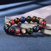 Colorful Liuli Glass Bead Luck Bracelet – Multicolored translucent glass beads with large pale blue focal bead, gold toggle clasp on white silk cushion, elevated diagonal