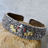 PiXiu Engraved Blessing Bracelet Bangle – detailed silver cuff with gold accents and red turquoise stones on rock