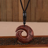 Red sandalwood peace buckle spiral pendant necklace with intricately carved cloud and key-fret patterns on warm reddish-brown wood disc with black braided cord and silver-inlaid accent bead on wooden stand
