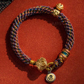 Om Mani Padme Hum Braided Bracelet – Multi-color woven cord with gold ruyi medallion and mantra pendant on red surface
