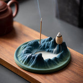 Ceramic Backflow Incense Burner – Blue-green mountain dish with smoke pooling in valley, teapot nearby, zen decor