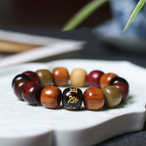 Wood Bead Bracelet – multi-wood barrel beads with gold Om focal bead on ceramic dish, zen style, wooden mala