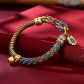 Zakiram Goddess Wealth Bracelet – Multicolor braided cord with gold bell, engraved beads and rectangular pendant on burgundy satin