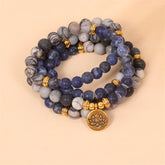 108 mala beads sodalite zebra jasper lotus bracelet triple-strand design with navy blue sodalite gray marbled jasper charcoal beads gold spacers and lotus flower pendant on beige background