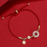 Adjustable red braided cord bracelet with white jade bi disc pendant, gold ruyi cloud charm with crystal accent and fortune blessing pendant on red background
