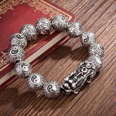 Tibetan Feng Shui PiXiu Silver Bracelet – Antique oxidized silver Pixiu charm with Tai Chi Bagua engraved beads on dark wood table with vintage red book
