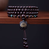 108 bead mala bracelet with polished red sandalwood beads, turquoise accent stones, gold-toned spacer beads and carved wood guru bead with gold lotus flower inlay on dark wood surface