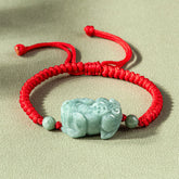 Jade PiXiu Knot Bracelet – Red braided cord bracelet with light green jade PiXiu on beige surface, protection jewelry
