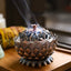 Lotus Incense Burner emitting smoke from perforated lid, vintage bronze on wood, enlightenment