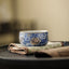Lotus Chrysanthemum Ceramic Tea Cup - Blue-white floral with gold rim on fabric mat, ceremonial
