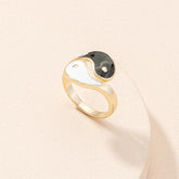 Yin Yang Adjustable Couple Ring - angled view of gold black white enamel symbol on cream surface, balance jewelry