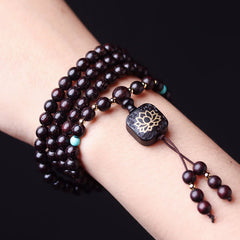Multi-wrap 108 bead red sandalwood mala bracelet worn on wrist with turquoise accent beads and carved lotus flower guru bead against pure black background