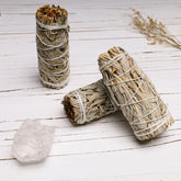 Three white sage smudge sticks with clear quartz crystal on white rustic wood