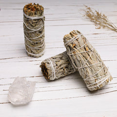 Three white sage smudge sticks with clear quartz crystal on white rustic wood
