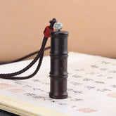 Ebony Wood Bamboo Prayer Box Necklace – Dark bamboo-segment pendant on cord with jade bead and red wrap, Chinese calligraphy book backdrop, low angle