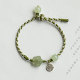 Plum Blossom Jade Flower Braided Bracelet – Olive green white twisted cord with pale jade flower bead and silver shou charm on white background, top-down flat lay
