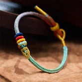 Five-Color Eight Thread Peace Knot Bracelet – Multicolor braided cord with turquoise gold red blue stacked ring knots and wrapped bead, brown fabric low side macro