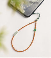 Olive Kernel Phone Chain – bamboo-style olive beads with jade and green stone charm beside floral phone, natural stone phone strap