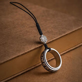 Mantra Phone Ring – silver spinning ring with black cord on vintage brown book, engraved symbols