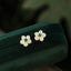 White Jade Flower Blessing Stud Earrings – Five-petal white jade flower earrings with green jade centers in gold settings, dark green velvet jewelry box, elevated side
