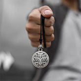 Taotie Copper Wealth Necklace – Silver taotie mask pendant on black cord held in hand, gray blurred background, frontal lifestyle shot