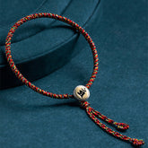 Chinese Zodiac Natal Buddha Bracelet – Multicolor braided cord with gold Sanskrit bead on dark teal fabric, spiritual healing bracelet