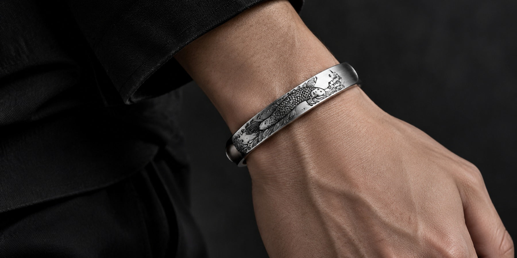 Brushed silver open cuff bracelet with koi fish engraving on a man's wrist