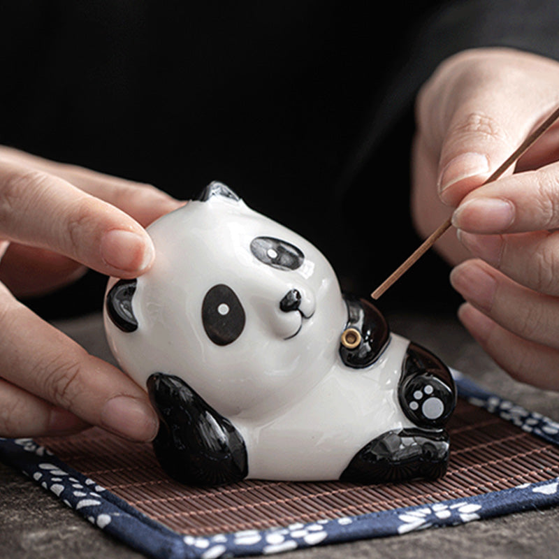 Hands placing incense stick into ceramic panda incense holder on patterned mat