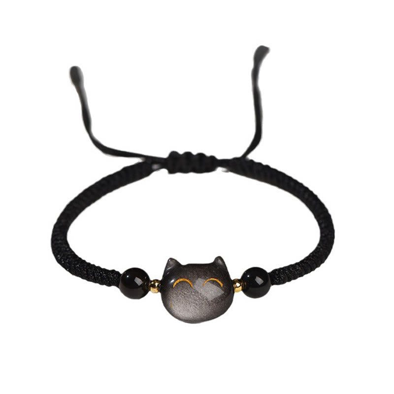 Adjustable black braided cord bracelet with obsidian cat face charm, golden eyes, black faceted beads and gold accents on white background