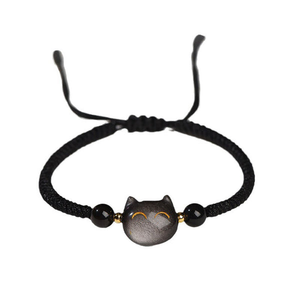 Adjustable black braided cord bracelet with obsidian cat face charm, golden eyes, black faceted beads and gold accents on white background