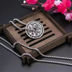 Antique Shan Gui Pendant – silver coin on wood tray with silver chain and pink blossoms, dark backdrop, traditional spiritual protection necklace