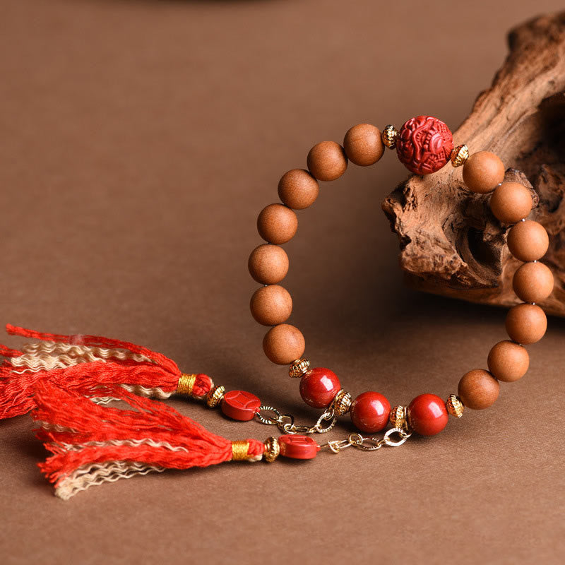 Peach Wood PiXiu Wealth Bracelet – Wood and red cinnabar bracelet with gold chain tassels on driftwood