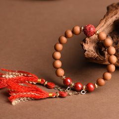 Peach Wood PiXiu Wealth Bracelet – Wood and red cinnabar bracelet with gold chain tassels on driftwood