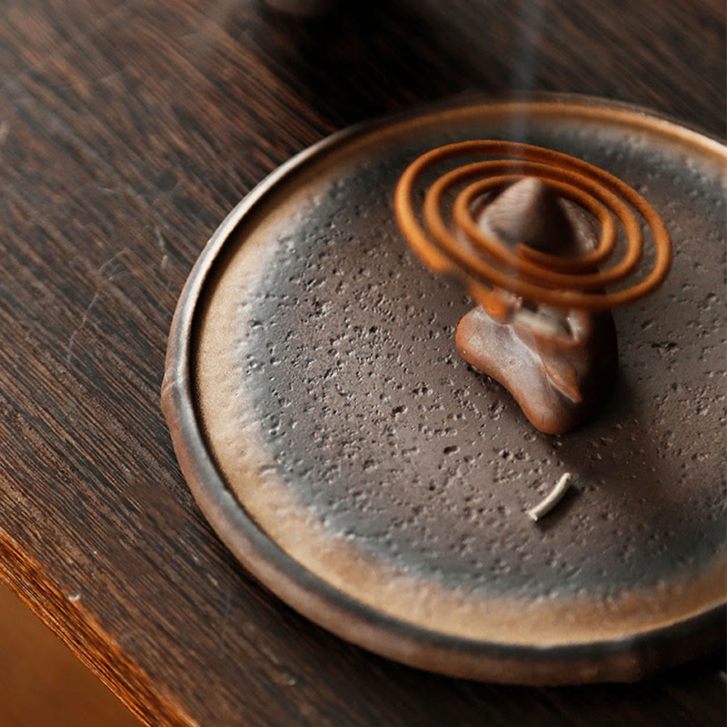 Charcoal ceramic dish with coil incense and stone holder on dark wood, healing