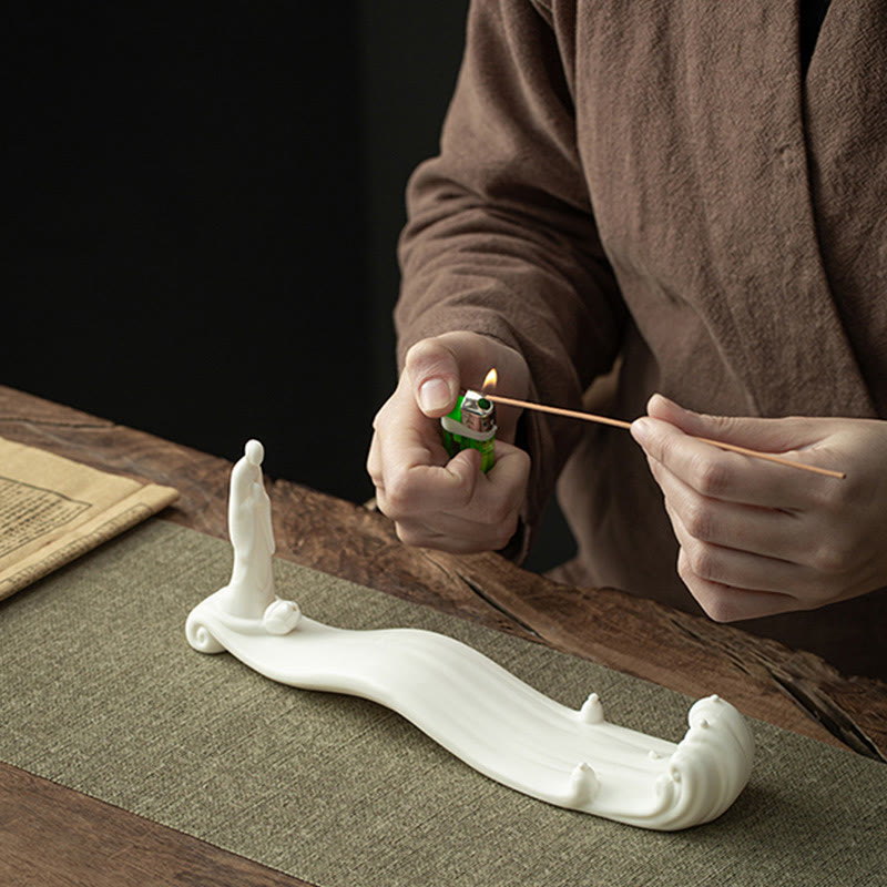 Buddha Monk Sea Wave Mountain Ceramic Incense Burner – Hands lighting incense stick on white ceramic wave holder with sage mat, meditation accessories