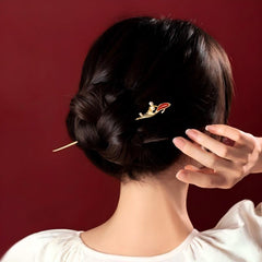 Koi Hairpin – styled in a low bun with hand touching hair, maroon studio background, daily wear