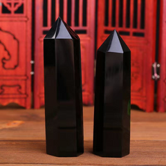 Two polished black obsidian crystal point towers on wooden surface, red decorative screen background, feng shui protection stones