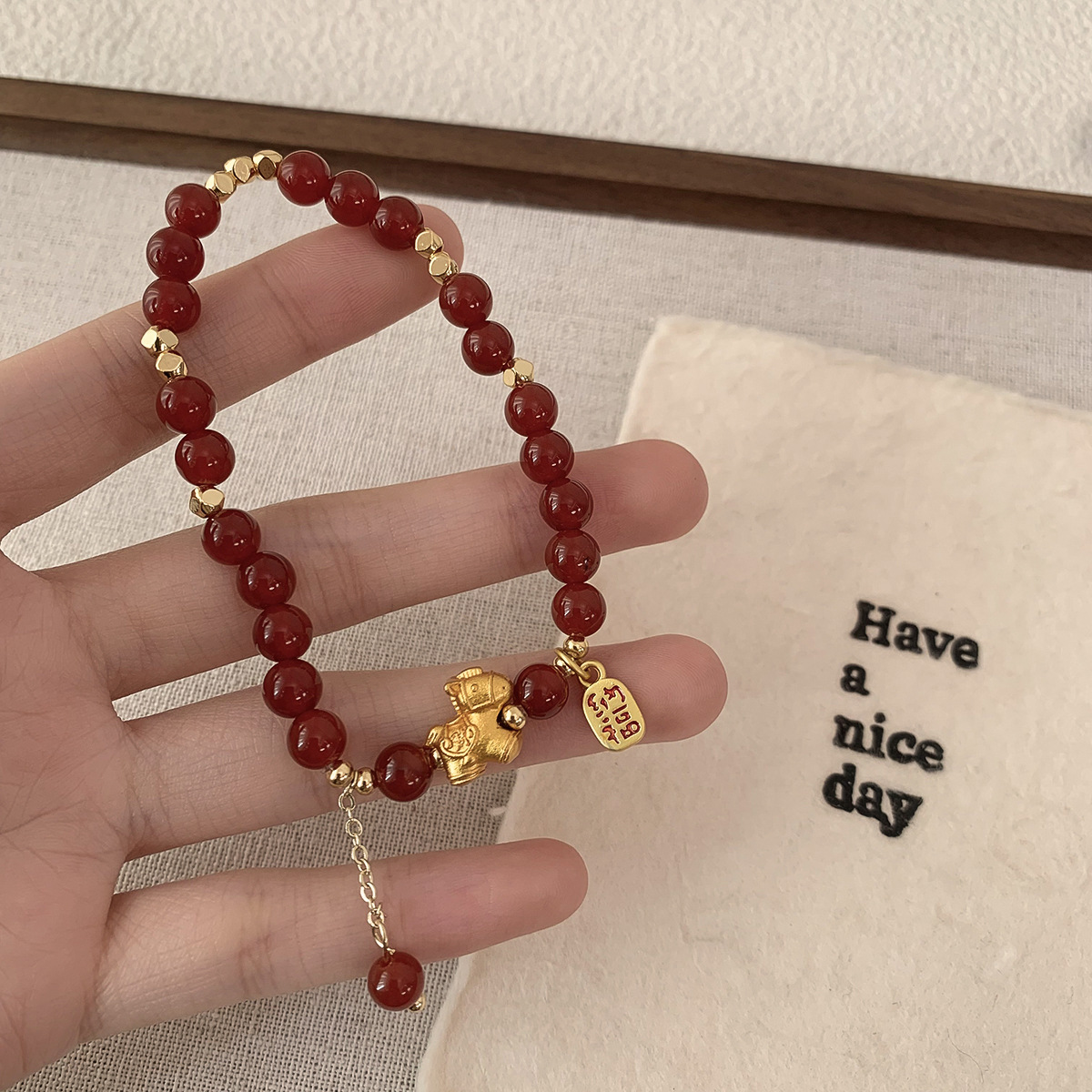 Horse Year Bracelet – hand holding red beads with gold horse and fortune pendant, gift bag beside