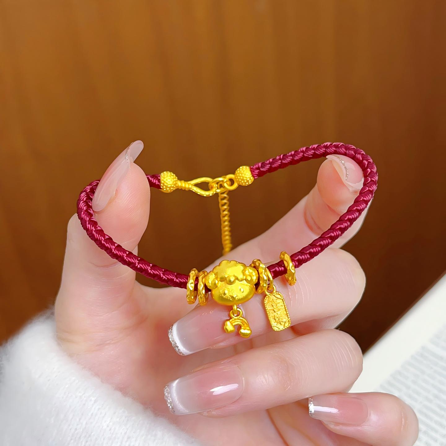 Ben Ming Nian Bracelet – gold ox charm held in manicured hand, brown wooden background, delicate