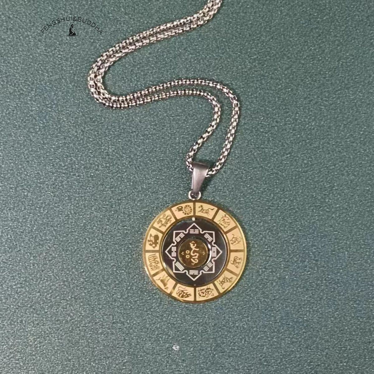 Zodiac Spin Necklace – flat lay with silver chain, gold zodiac ring dark center gold text, teal backdrop, Om Mani Padme Hum