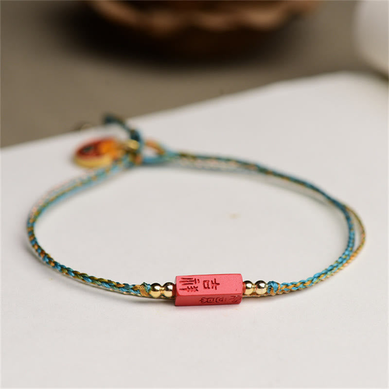 Cinnabar Bracelet - Red carved bead with gold characters on turquoise cord, white background