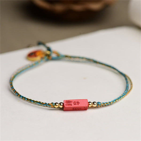 Cinnabar Bracelet - Red carved bead with gold characters on turquoise cord, white background