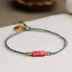 Cinnabar Bracelet - Red carved bead with gold characters on turquoise cord, white background