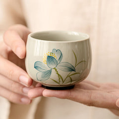 Hand Painted Lotus Tea Cup – held in two hands showing blue lotus bloom, yellow center, sage stems, zen calming